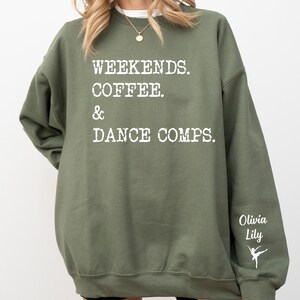 Op de afbeelding: Groen sweatshirt met de tekst "Weekends. Coffee. & Dance Comps." in wit. De rechtermouw heeft de tekst "Olivia Lily" en een wit silhouet van een danseres.
