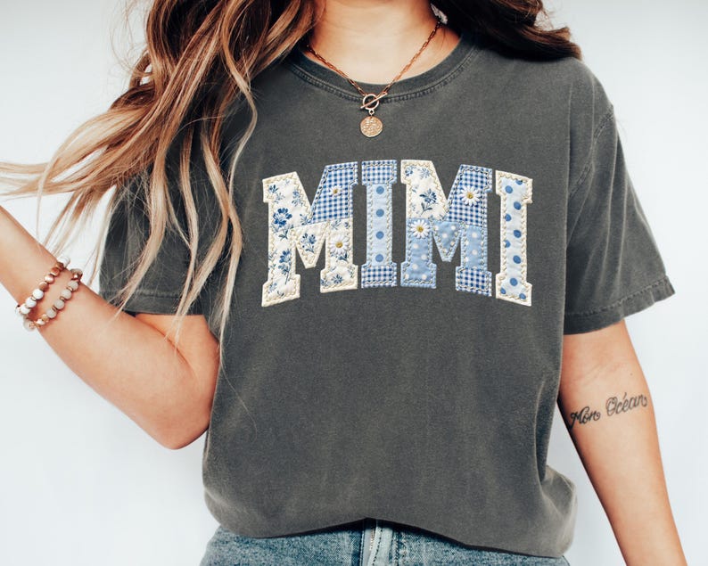 K&ouml;nnte beinhalten: Dunkelgraues T-Shirt mit dem Wort "MIMI" in einem Patchwork-Design. Die Buchstaben sind in blau-wei&szlig;en Blumen- und Vichy-Mustern gehalten. Das Shirt hat kurze &Auml;rmel und einen Rundhalsausschnitt.