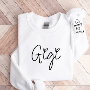 May include: White sweatshirt with the word "Gigi" written in black cursive with two small hearts above the word. The sleeve has the names "Oliver", "Lily", and "Emma" written in black cursive with a heart next to each name.