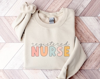 May include: A beige sweatshirt with the text "registered NURSE" in colorful letters. The letters are outlined in black and have a pastel color scheme.