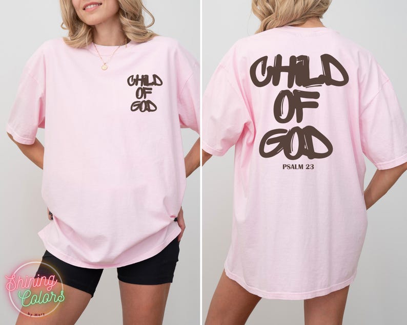 May include: Light pink oversized t-shirt with the words "CHILD OF GOD" printed in brown on the front and back. The back also includes "PSALM 23" in brown. The shirt is a comfortable, casual style.