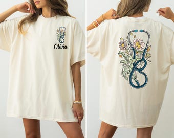 May include: A cream-colored t-shirt with a floral design featuring a stethoscope and the name "Olivia" printed on the front.