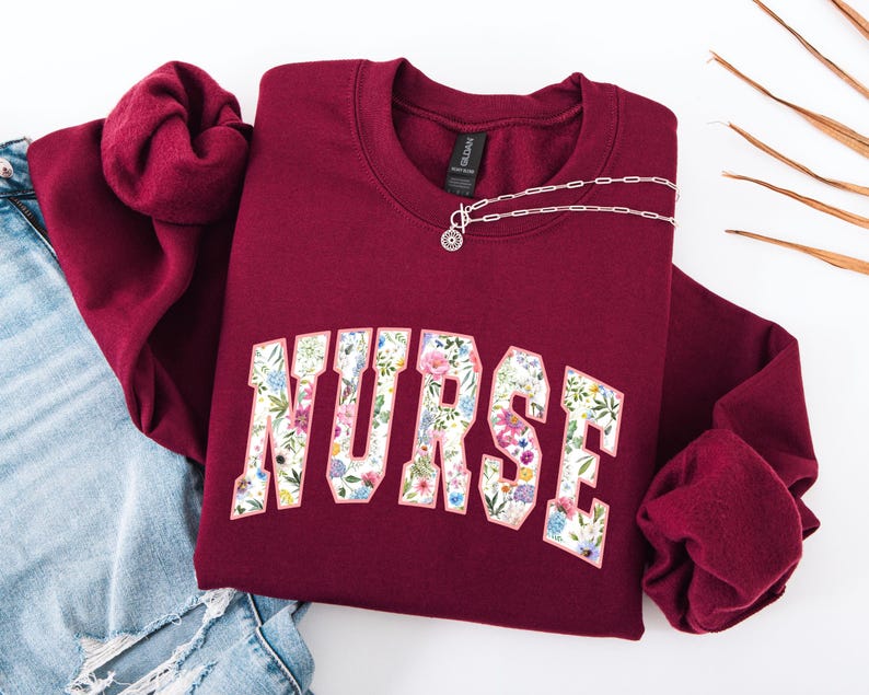 May include: Burgundy sweatshirt with a floral print of the word "NURSE" on the front.
