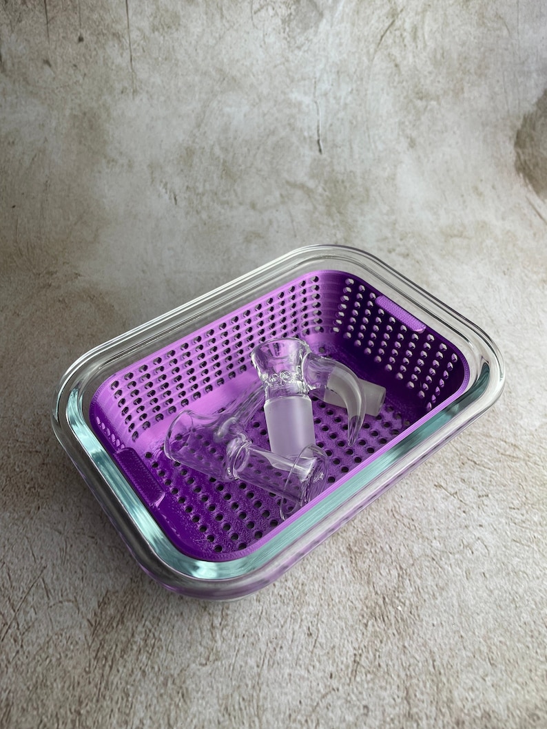 May include: A clear glass and purple tray containing several glass pieces. The tray features a purple perforated insert and a clear glass border. The glass pieces are of different shapes and sizes.