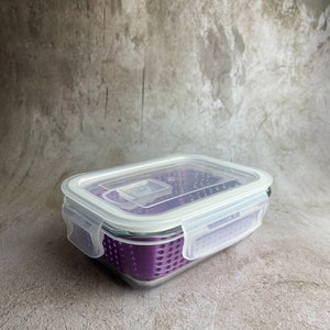May include: A rectangular glass food storage container with a clear lid and purple interior. The lid has white plastic clips on each side. The container is designed for food storage and is suitable for kitchen use.