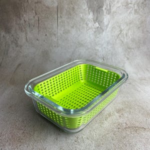 Może przedstawiać: Prostokątny pojemnik z przezroczystego szkła z wyjmowanym wkładem w formie durszlaka z jasnego, limonkowego plastiku. Wkład posiada siatkę małych kwadratowych otworów drenażowych wzdłuż dna i boków, dopasowaną do szklanej podstawy.