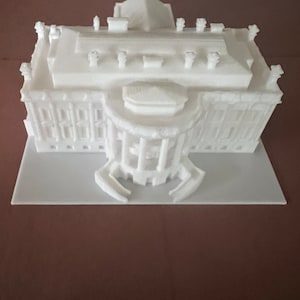 Peut inclure: Modèle 3D imprimé en blanc d'un bâtiment avec une façade détaillée et un toit plat. Le modèle est posé sur une base blanche.