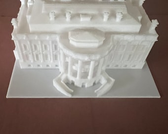 May include: A white 3D printed model of a building with a detailed facade and a flat roof. The model is sitting on a white base.
