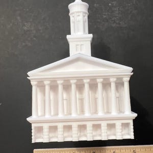 May include: White 3D printed model of a building with a tall, narrow tower and a columned facade. The model is approximately 5 inches wide and 6 inches tall.