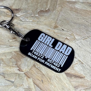 Könnte beinhalten: Schwarzer rechteckiger Schlüsselanhänger mit dem Text "GIRL DAD" und einem Barcode-Design. Unter dem Barcode stehen die Worte "SCAN FOR PAYMENT" und eine Reihe von Zahlen. Der Schlüsselanhänger ist an einem silbernen Schlüsselring und Verschluss befestigt.