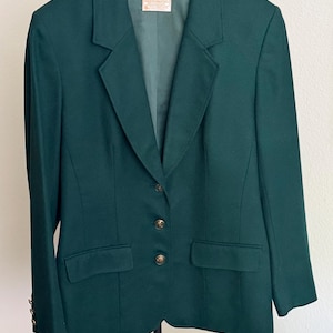May include: A dark forest green blazer featuring a notched lapel, three gold-toned buttons down the front, and two flap pockets. The interior label reads Pendleton, and the garment is displayed on a black Barneys New York branded hanger.