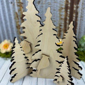May include: A set of five wooden cutout trees, each with a unique shape and size. The trees are painted in a natural wood color and have a black outline. The set includes a small bird cutout.
