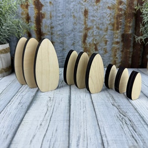 May include: A set of nine wooden oval shapes with black edges. The ovals are arranged in size order from largest to smallest.