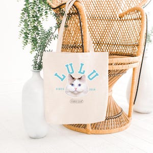 May include: A beige tote bag with a blue and white cat illustration and the text "LULU SINCE 2016" in blue. The text "STUDIO CELLO" is printed in black below the cat.