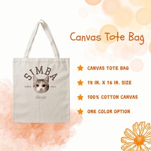 May include: A beige canvas tote bag with a cat's face and the text "SIMBA" printed on the front. The text "SINCE 2018" is printed below the cat's face. The bag is 15 inches by 16 inches and made of 100% cotton canvas.