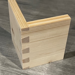Pu&ograve; includere: Un primo piano di un giunto d'angolo in legno con pi&ugrave; pezzi che si incastrano. Il giunto &egrave; realizzato in legno chiaro, liscio e lucido.