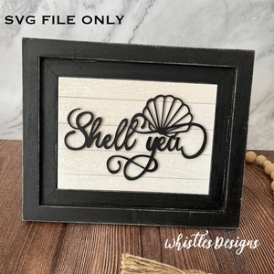 May include: Black and white sign with the text "Shell yeah" and a seashell design. The sign is framed in a black frame and is sitting on a wooden surface.
