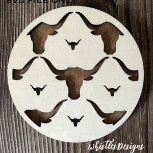Puede incluir: Un letrero de madera circular blanco con una silueta marrón de una cabeza de toro con cuernos repetida en un patrón. El texto "Whistles Designs" está en la parte inferior del letrero.