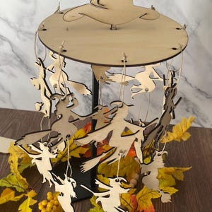 May include: Wooden Halloween mobile featuring witch silhouettes hanging from a circular base and a witch hat. The text "SVG FILE ONLY" is at the top. The mobile is decorated with fall leaves and the text "whistles designs" is at the bottom.