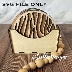 May include: Set of six wooden coasters with a zebra stripe pattern, in a wooden holder. The coasters are stacked in the holder, and the holder is sitting on a wooden surface. The text "Whistles Designs" is visible on the surface.