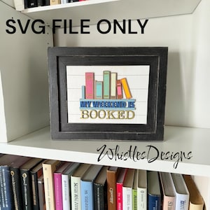 May include: A black framed sign featuring a white background with horizontal lines and a colorful row of books on a shelf. The text reads "MY WEEKEND IS BOOKED" in blue and gold lettering. The image also includes the text "SVG FILE ONLY".