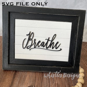 May include: A black framed sign with a white background and the word "Breathe" written in black cursive script.