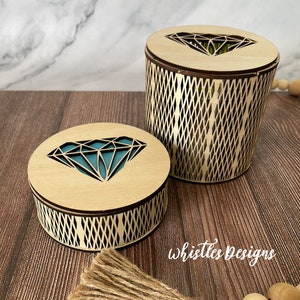 Könnte beinhalten: Zwei Holzkisten mit Diamant-Ausschnitten. Die Kisten sind aus hellem Holz und haben ein geometrisches Muster an den Seiten. Die kleinere Kiste hat einen türkisfarbenen Diamant-Ausschnitt, während die größere Kiste einen grünen Diamant-Ausschnitt hat. Die Kisten stehen auf einer Holzoberfläche.