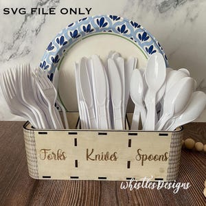 Könnte beinhalten: Ein hölzerner Besteck-Organizer mit den Worten "Forks", "Knives" und "Spoons" auf der Vorderseite. Der Organizer enthält weiße Plastikgabeln, -messer und -löffel. Im Hintergrund befindet sich ein Pappteller mit blauem Blumenmuster. Der Text "SVG FILE ONLY" steht oben.