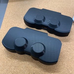 May include: Two black plastic game controllers with two buttons each. The controllers are designed to fit in the palm of your hand.