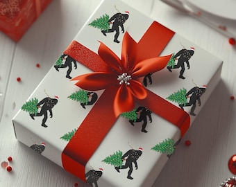 Puede incluir: Un regalo envuelto con un lazo rojo y un patrón de Bigfoot llevando un árbol de Navidad. El regalo está sobre una superficie de madera blanca, rodeado de adornos rojos y otros regalos envueltos.