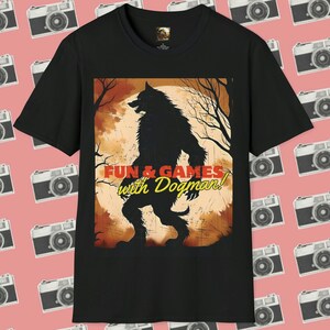 May include: Black t-shirt featuring a graphic print of a werewolf standing in front of a full moon. The text "Fun & Games with Dogman!" is printed in red and yellow on the shirt.