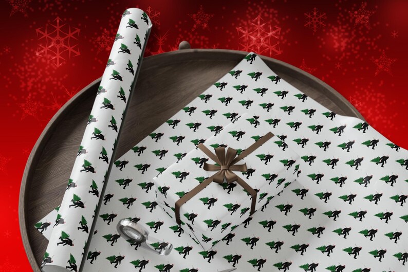 Puede incluir: Papel de regalo blanco con un patr&oacute;n repetitivo de siluetas negras de una criatura cargando un &aacute;rbol de Navidad verde. El conjunto incluye un tubo de papel enrollado, una hoja plana y una caja peque&ntilde;a envuelta con una cinta marr&oacute;n.