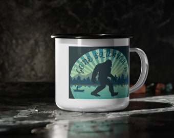Puede incluir: Taza de camping de esmalte blanco con borde y asa negros. La taza presenta un gráfico de un Bigfoot caminando por un bosque con el texto "Gone Squatchin'" en un esquema de colores azul y verde.