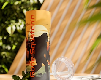 May include: A black and orange stainless steel tumbler with a graphic of a Bigfoot walking through a forest at sunset. The tumbler has the text "Gone Squatchin'" printed on the side.