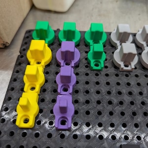 May include: Assortment of colourful plastic knobs in green, yellow, purple, and grey. The knobs are arranged in rows on a black pegboard.