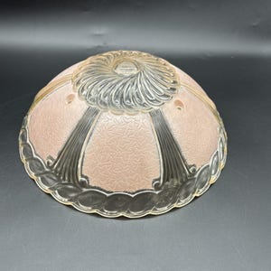 May include: A vintage glass lampshade with a pink, textured interior and clear, decorative exterior. The shade features a floral pattern and a scalloped edge. The top has a clear, swirling design.