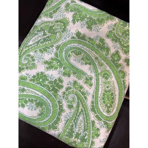 May include: Folded fabric with a white background and a repeating paisley pattern in shades of green. The paisley design features a teardrop shape with intricate detailing and a lighter green outline. The fabric appears to be cotton or a similar material.