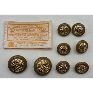 May include: A collection of vintage Pendleton buttons in various sizes, featuring a gold emblem on a brown background. A Pendleton label is also present, with text that reads "Warranted to be a Pendleton".