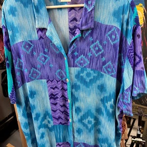 May include: A vintage button-down shirt in shades of blue and purple, with a geometric pattern. The shirt has short sleeves and a collared neckline. The brand name "teddi" is visible on the label.