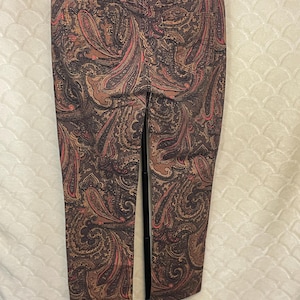May include: Brown paisley print pants with a classic design. The pants feature a detailed pattern in shades of brown, tan, and red. The pants are hanging on a black hanger.