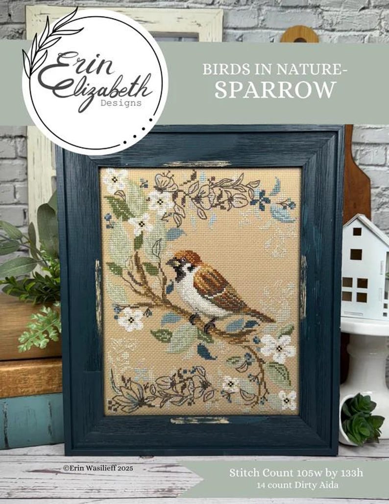 May include: Cross stitch pattern of a sparrow perched on a branch with white flowers. The pattern is framed in a dark blue frame and the text "BIRDS IN NATURE - SPARROW" is above the frame. The text "Erin Wasilieff 2025" is below the frame. The stitch count is 105w by 133h and the fabric is 14 count Dirty Aida.