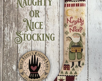 May include: A red and green Christmas stocking with a white embroidered design of a Santa Claus holding a house and the text "Naughty or Nice?"  The stocking is on a white wood background.