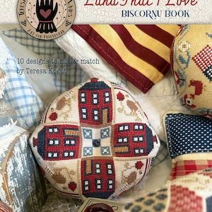 May include: A Biscornu book titled "Land That I Love" by Teresa Kogut. The cover features a stitched, round pincushion with red houses and blue accents. The image includes other stitched items and the text "10 designs to mix & match".