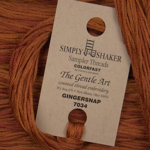 May include: A skein of brown embroidery floss with a label that reads "SIMPLY SHAKER Sampler Threads COLORFAST by industry standards The Gentle Art counted thread embroidery PO. Box 670 New Albany, Ohio 43054 GINGERSNAP 7034"