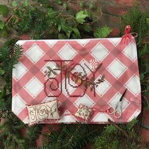 May include: A rectangular project bag with a red and white plaid pattern featuring the embroidered word JOY in dark red thread. Included are a small rectangular pincushion, a square pincushion, and a pair of small scissors with a red ribbon.