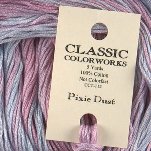May include: Close-up of Classic Colorworks embroidery floss in the color "Pixie Dust." The floss is a blend of pink, lavender, and light blue. The label indicates it is 100% cotton and 5 yards in length.