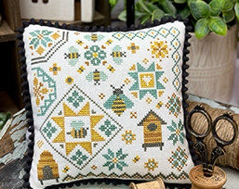 May include: A white cross-stitch pillow with a bee and honeycomb design. The pillow has a black trim and is sitting on a wooden tray with spools of thread. The text "Honeybee Quaker" is at the top of the image and "Primrose Cottage Stitches" is at the bottom.