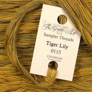 May include: A spool of The Gentle Art Sampler Threads in the color Tiger Lily, shade 0115. The thread is a deep golden yellow with a slight green undertone. The label is white with brown text and a small bird illustration.