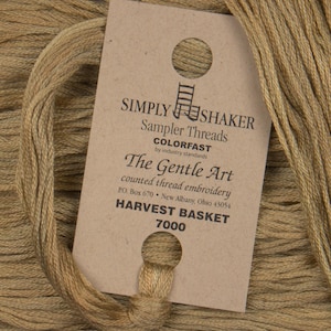 May include: A brown skein of embroidery floss with a label that reads "Simply Shaker Sampler Threads Colorfast by industry standards The Gentle Art counted thread embroidery PO. Box 670 New Albany, Ohio 43054 Harvest Basket 7000"