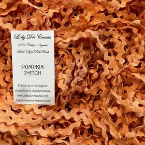 May include: Close-up of orange rick rack ribbon, with a wavy, textured design. A white label reads "Pumpkin Patch" and details about the ribbon's cotton content and length.